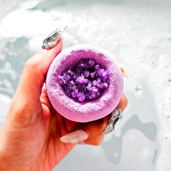 Cosmo lavender bath bomb with vibrant purple crystals held over a bubble bath