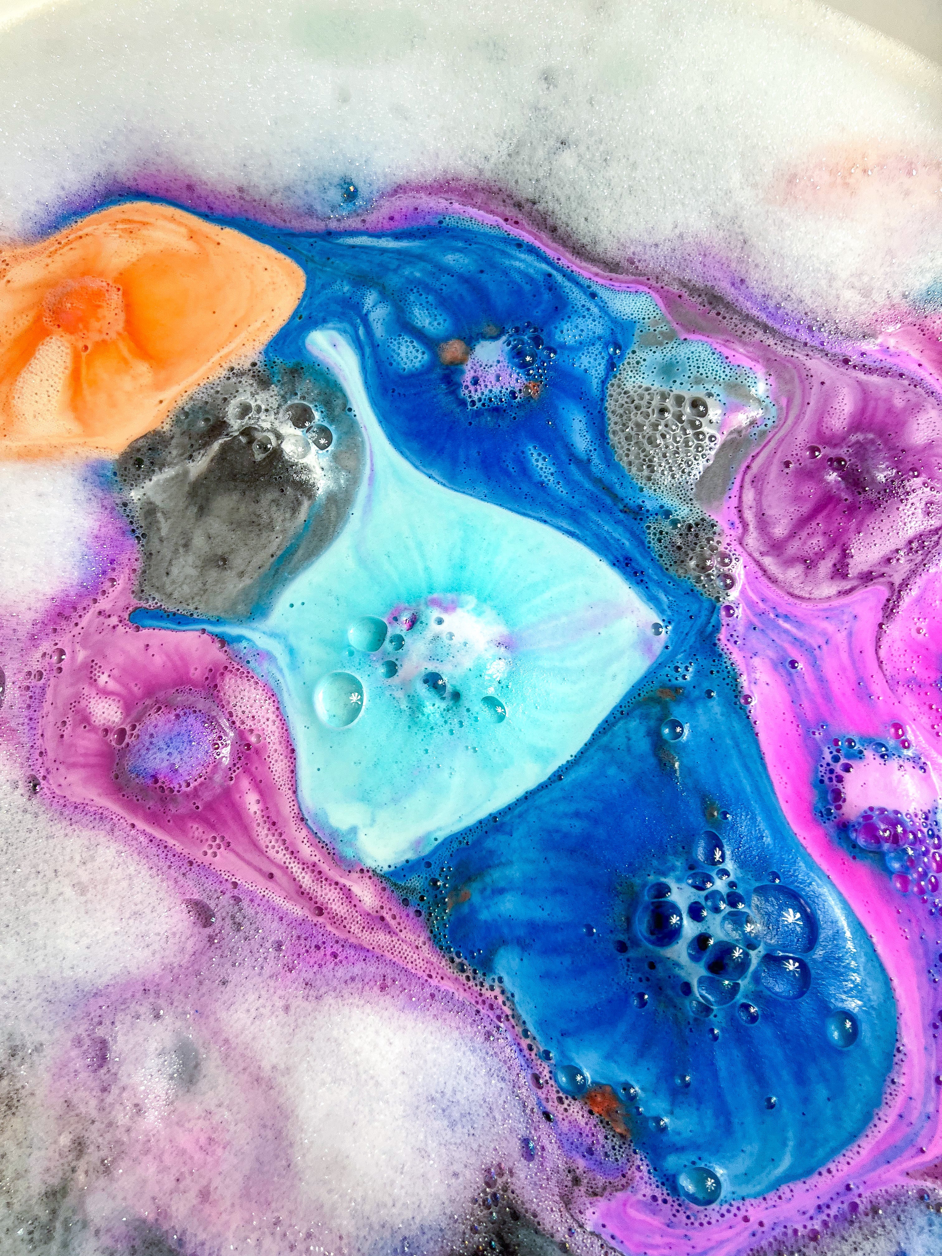 Multiple colours of galaxy bath bomb swirl in water and foam