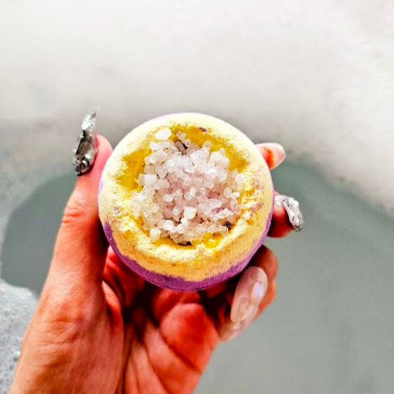 Starburst lemongrass bath bomb with Epsom salt held over a bathtub